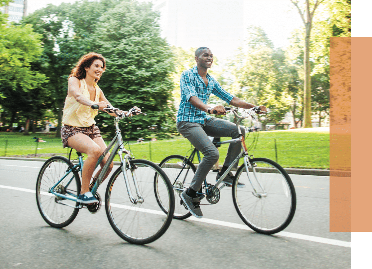 Young couple riding bikes down a paved bike path in the summer surrounded by trees and greenery